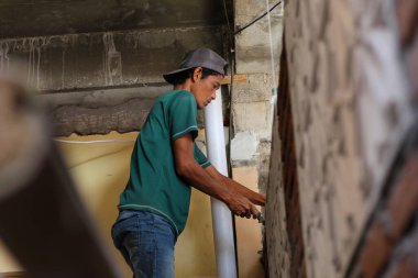 Asyalı erkek inşaat işçisi, içeride duvar inşa ederken kırmızı kil tuğla kesmek için metal bir mala kullanıyor. Güneydoğu Asya 'da geleneksel ev inşaatında el işçiliği. 6 Ağustos 2025, Lombok, Endonezya.