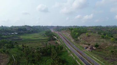 Arka planda bir sürü ağaç ve ev olan bir yol. Birkaç araba ve motosikletin geçtiği yol.