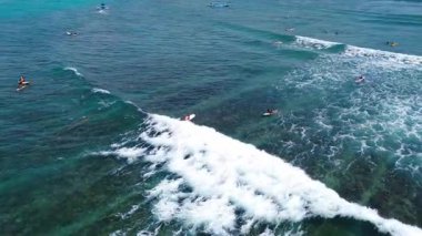 Açık yeşil okyanusta sörf tahtası üzerinde sörf yapan bir sörfçünün insansız hava aracı görüntüsü. Sörfün ham enerjisini ve hareketini yukarıdan yakalar.