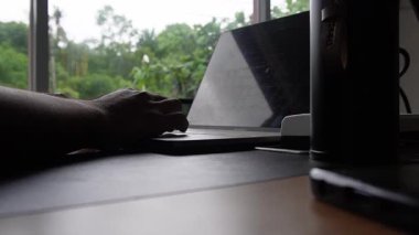 Eller dizüstü bilgisayarda yazıyor. Laptop siyah bir masanın üzerinde. Küçük bir siluet ve pencerenin manzarası ile
