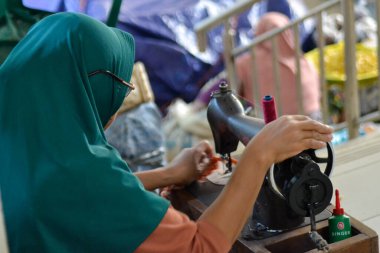 Kadın bir parça bez dikiyor. O bir Singer dikiş makinesi kullanıyor. Praya 28 Ağustos 2025. Lombok Endonezya