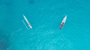 Turkuaz denize demirlenmiş iki boş ahşap kayığın, sakin bir şekilde berrak tropikal okyanus suyunda yüzen insansız hava aracı görüntüsü..