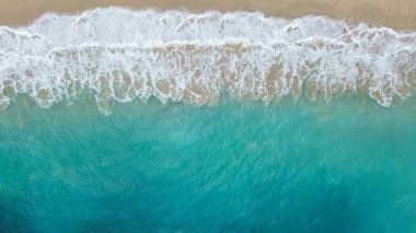 Turkuaz okyanus dalgalarının kumlu kıyılarda kırılıp köpük ve dokudan oluşan doğal deniz manzarasının insansız hava aracı çekimi..