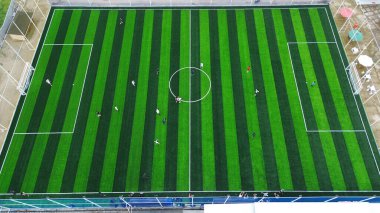 High angle view of people playing a soccer match on a vibrant green striped pitch. An aerial perspective on sports, fitness, and teamwork.