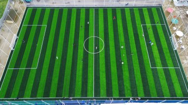 Top down drone shot of a striped green football pitch. Players compete in a local match, a concept for teamwork, sport, and an active lifestyle.