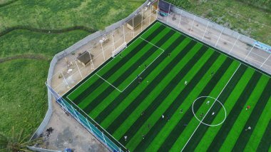 High angle drone shot of a community football game on a green striped pitch. Team playing in a countryside setting, a concept of sport and recreation.