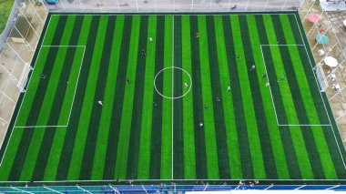 Top down drone shot of a green striped football pitch. People play a local game, representing teamwork, strategy, and a healthy lifestyle.