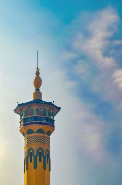 Bir caminin minaresine karşı mavi gökyüzü ve bulutlu alacakaranlık.