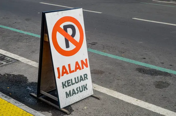 a board containing a sign that no parking is permitted on the side of the road. Translation on board \