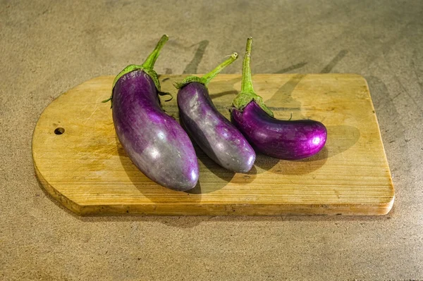 Üç mor patlıcan ya da tahta arka planda kesme tahtasının üzerinde duran Solanum Melongena.