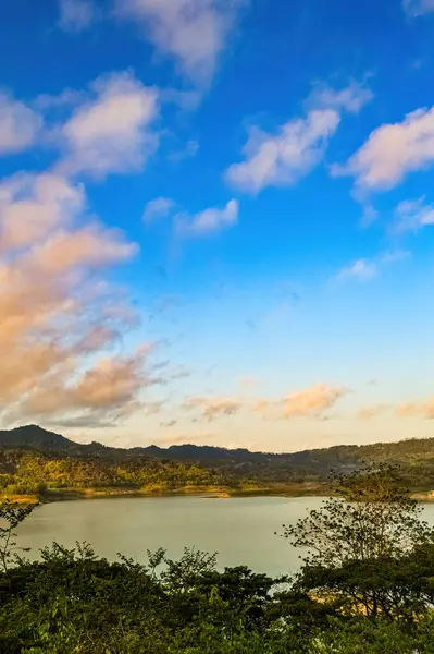 Güneşli bir sabahta Endonezya 'da dağlarla çevrili doğal bir gölün panoramik portresi