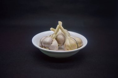 Sade beyaz bir tabakta sade siyah bir zeminde izole edilmiş bir avuç sarımsak.