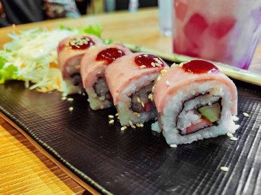 Siyah tabakta bir rulo pişmiş somon suşi.