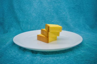 Beyaz bir tabakta turkuaz kumaşlı üç dilim peynirli kek.