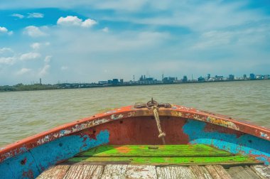 Arkasında sanayi silüeti olan ahşap bir teknenin önünde.