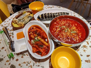 Kore yemekleri, kimbap, ramyeon, tteokbokki ve gimmari içeren bir masa.