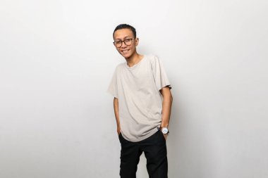 Gözlüklü ve beyaz gömlekli bir adam gülümsüyor. Bir saat takıyor ve elleri cebinde.