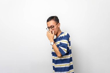 Gözlüklü ve saati olan bir adam beyaz bir arka planın önünde duruyor. Kameradan kafasını çeviriyor ve dalgın bir ruh halinde.