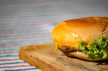 Et, domates sosu, mayonez ve salatayla dolu bir sığır peyniri burgeri kesme tahtası ve piknik tarzı kumaş. Lezzetli görünüyor ve aç mideler yapmak cazip geliyor.