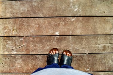 Eski, gri ahşap tahta zeminde duruyor. Ayaklarına bakıyorum. sandalet giyiyor.