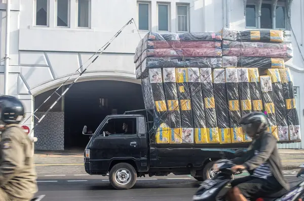 stock image a Mitsubishi L300 pickup truck carrying an overloaded and over dimensional load in the form of a pile of spring beds quite high on the Surabaya highway which is dangerous, Indonesia, 20 June 2024.