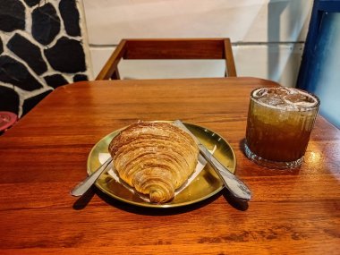 Lüks bir kafe veya restoranda ahşap bir masada servis edilen bir tabak kruvasan ekmeği ve bir bardak çay, bira veya viski.