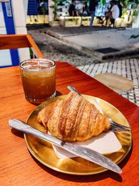 Lüks bir kafe veya restoranda ahşap bir masada servis edilen bir tabak kruvasan ekmeği ve bir bardak çay, bira veya viski.