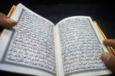 Elle tutulan altın kenarlı açık Kur 'an kitabı, görünür Arapça yazılar, İslami inanç ve ruhaniliği sembolize ediyor. Arapça çeviri: Kutsal Kuran (Müslümanlığın kutsal kitabı))