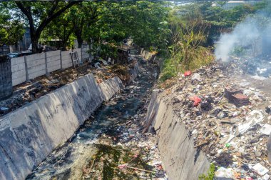 Çöp ve molozlarla dolu kirli şehir kanalı, yanan atıklardan yükselen duman, çevre sorunlarını vurguluyor, Endonezya, 18 Eylül 2024.