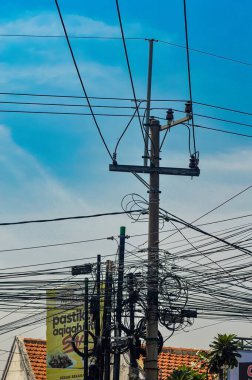 Açık gökyüzüne karşı elektrik direğindeki karmaşık kentsel kablo ağı, reklam panoları ve yeşillik, Endonezya, 18 Eylül 2024.
