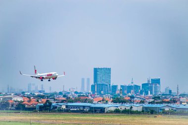 Surabaya şehir manzarası ile Juanda Uluslararası Havalimanı 'na inen Lion Air uçağı, modern havacılık ve kentsel büyümeyi yakalıyor, Surabaya, 22 Eylül 2024.