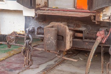 Paslı bir tren bağlayıcısını zincir ve hortumlarla kapatın. Detaylı mekanik parçaları gösterin ve kullanılmaktan yıpranın.