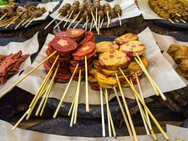 Bir pazarda parşömen kağıdında çeşitli renkli ve çeşitli malzemelerle gösterilen şiş yiyecekler.