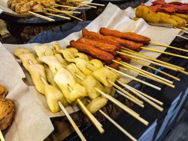 Balık köftesi ve sosis de dahil olmak üzere çeşitli sokak yiyecekleri bir markette parşömen kağıdında sergileniyor.