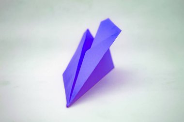 Beyaz arka planda, özgürlük ve uçuşu sembolize eden mor kağıt bir uçak. Seyahat, macera ya da motivasyonel kavramlar için uygundur