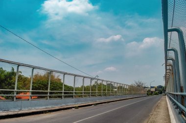 Metal parmaklıkları ve parlak mavi gökyüzünün altında çitlerle örülmüş bir yaya köprüsü. Kentsel altyapı ve ulaşım temaları için ideal