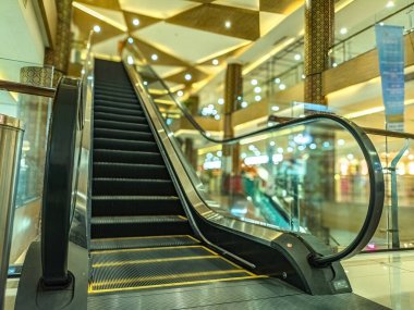 Zarif dekorları ve cam parmaklıkları olan, ışıl ışıl bir alışveriş merkezinde, üst kata çıkan modern bir yürüyen merdiven.