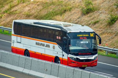 Bir Harapan Jaya şehirlerarası otobüsü, modern tasarım ve konfor özelliklerini sergileyerek paralı bir yolda seyahat eder. Endonezya ulaşım ve seyahat hizmetleri hakkında makaleler için ideal. Endonezya, 31 Ekim 2024