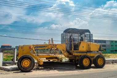Sarı bir Komatsu GD405A motorsikletli, açık mavi gökyüzünün altındaki bir inşaat sahasında park halinde. Bu resim inşaat, ağır makineler ve endüstriyel Endonezya için uygundur, 31 Ekim 2024