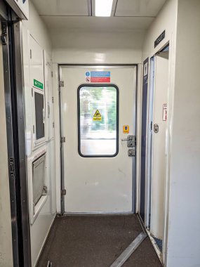 Kapı camında güvenlik levhası olan bir tren vagonunun iç bağlantısı modern tren özelliklerini vurguluyor. Endonezya, 16 Kasım 2024