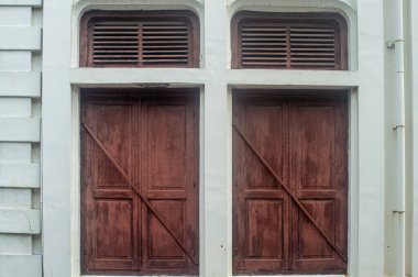 Eski bir binanın ön cephesinde üst havalandırma panelleri olan eski ahşap kapılar klasik mimari tasarım sergiliyor.