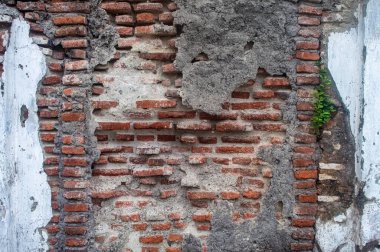 Eski, yıpranmış tuğla bir duvar. Parçalanmış alçı parçaları ve açıkta kalmış kırmızı tuğlalar. Çürüme ve yaşlanma belirtileri gösteriyor.
