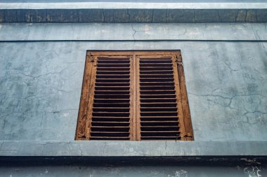 Çatlak, soluk mavi bir duvarda eski, yıpranmış ahşap bir pencere panjuru. Kırsal cazibe ve eskimiş doku onu klasik ve mimari fotoğrafçılık için büyüleyici bir konu haline getiriyor.
