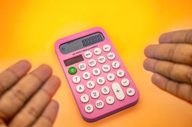 Ekranında 1000.000 gösteren pembe bir hesap makinesi iki el arasında canlı turuncu bir arka plana karşı tutulur.