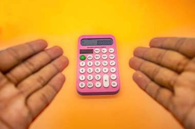 Ekranında 1000.000 gösteren pembe bir hesap makinesi iki el arasında canlı turuncu bir arka plana karşı tutulur.