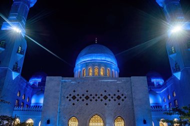 Surakarta, Solo 'daki Şeyh Zayed Büyük Camii' nin aydınlatılmış minaresinin çarpıcı bir gece görüntüsü. Mavi ışıklandırma karmaşık mimari detayları vurguluyor, büyüleyici bir görüntü yaratıyor.