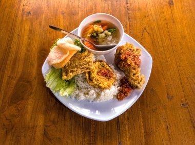 Rengarenk sebzeler, etler ve tahıllarla dolu beyaz kare bir tabak ahşap bir masaya yerleştirilir ve dengeli bir diyet için mükemmel taze ve iştah açıcı bir yemek sunulur.