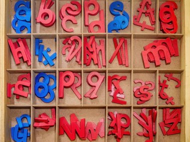 A wooden box with compartments containing colorful wooden letters in red and blue, arranged in a random order. Ideal for educational and playful activities clipart