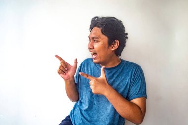 Mavi tişörtlü bir adam, iki eliyle, ters yönleri gösteren şakacı bir jest yapıyor. Sade beyaz arka plan deneği açıkça öne çıkarır ve bir sürpriz unsuru yakalar.