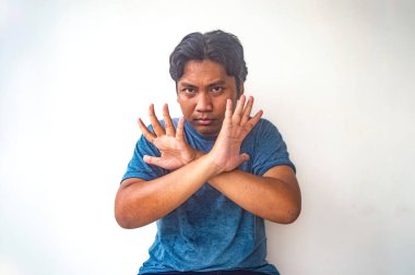 Mavi gömlekli bir adam, çapraz kolları ve beyaz bir arka planda açık elleri olan yasaklayıcı bir jest yapıyor. Bu resim reddetme veya reddetme kavramlarını göstermek için kullanışlıdır